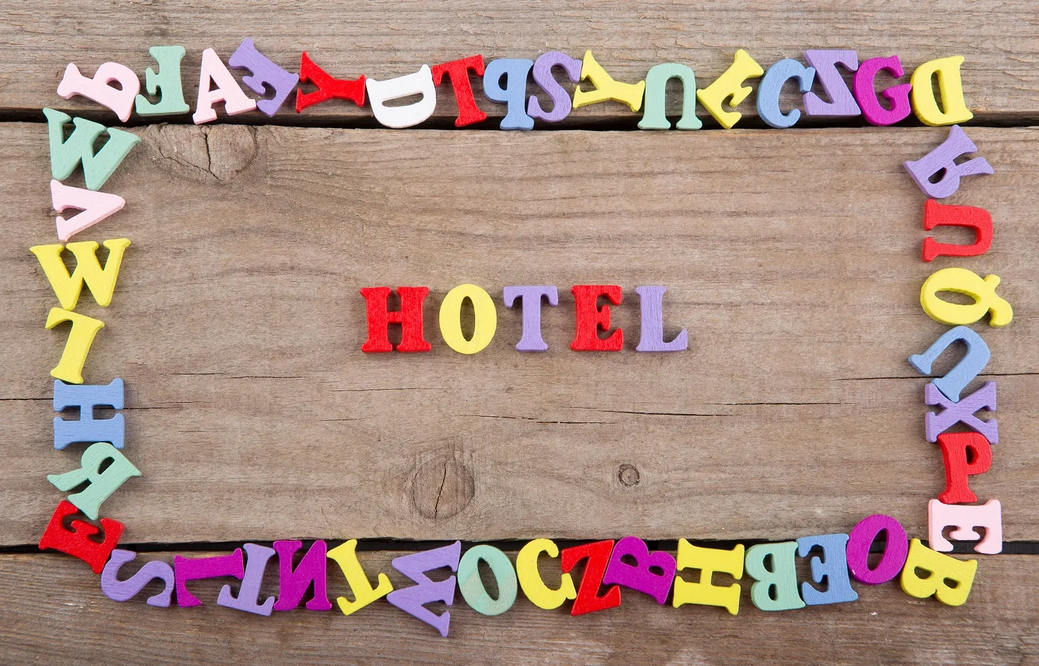 gestion-hotelera-letras-madera Hotel colorido formado por letras de madera sobre fondo rústico, simbolizando la gestión hotelera eficiente.