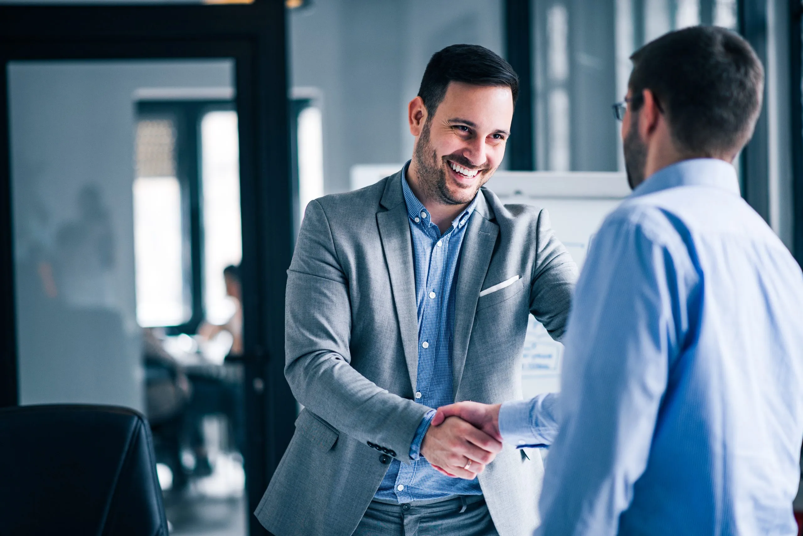 negocios-exitosos-partner-microsoft Dos hombres de negocios sonrientes estrechando manos, simbolizando el éxito y la colaboración de un partner de Microsoft Dynamics 365.